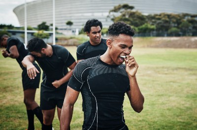On a sports pitch, a boy in athletic kit removes a mouthguard from his top arch