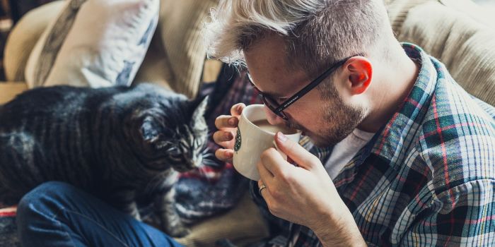 A man sitting on a sofa with his cat, drinking coffee