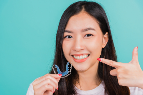 Smiling woman holds metal removable braces nest to her face to show the wires and shape outside of her mouth